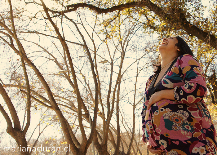 Embarazada riéndose a carcajadas junto a unos árboles